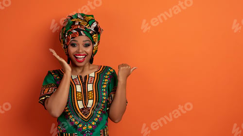 Preview: Excited young black woman in african costume showing nice offer