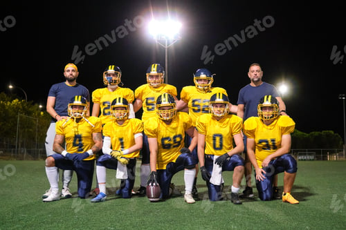 Preview: American football team and coaches posing on field at night