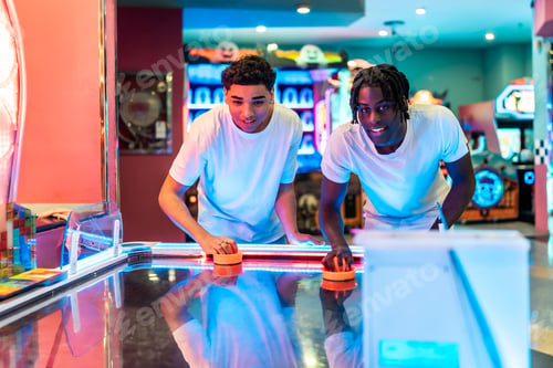 Preview: Two friends playing air hockey in amusement arcade