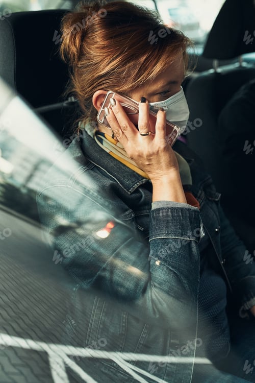 Preview: Woman talking on phone using smartphone sitting in a car wearing the face mask