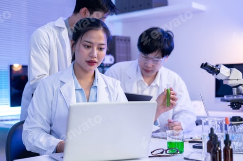 Preview: Asian woman scientist researcher holding test tube looking at laptop aside coworkers at table in lab