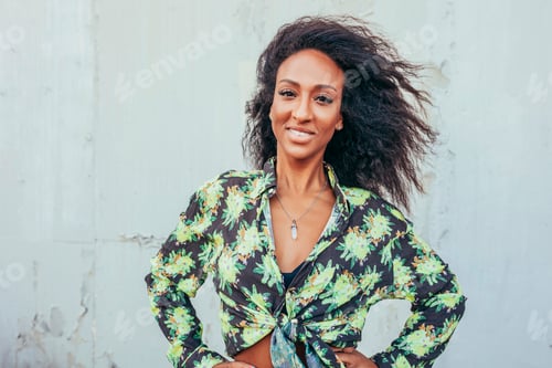 Preview: Stylish smiling afro woman near grey wall outdoors
