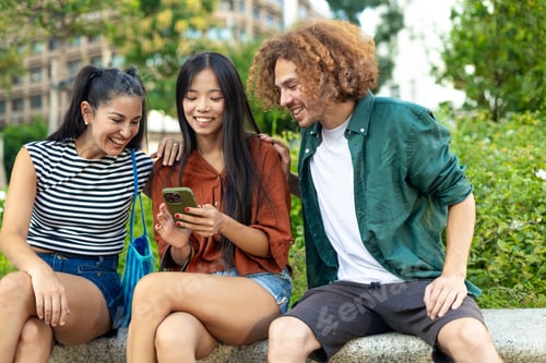 Preview: Group of friends laughing together while using smartphone in a park
