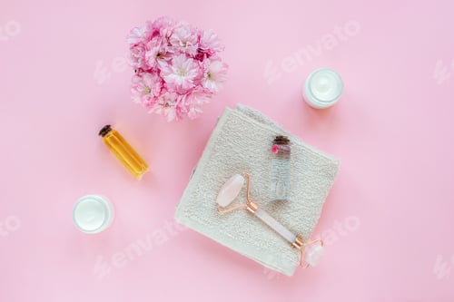 Preview: Spa accessories with flowers, oils, cream and facial roller on pink background. Top view, flat lay