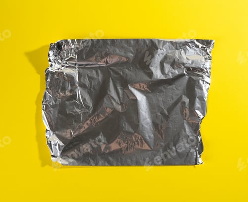 Preview: Crumpled sheet of gray foil for packaging products with torn edges on a yellow background,