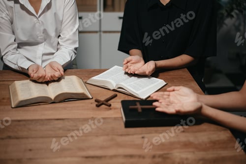 Preview: Group of Christians sit together and pray around a wooden table with blurred open Bible pages