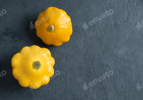 Preview: two yellow bush pumpkins on a dark textured background. Top view and copy space