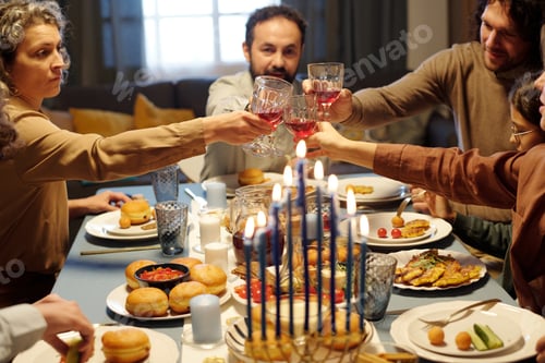 Preview: Members of large Jewish family clinking with wineglasses over served table