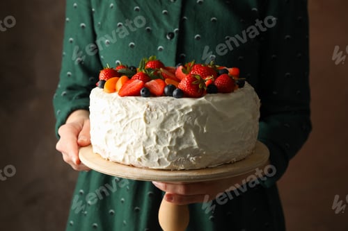 Preview: Woman holds berry cream cake against brown background. Delicious dessert
