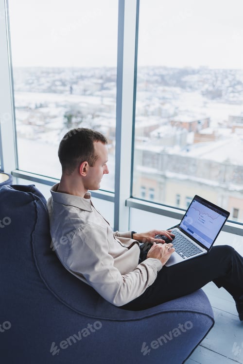 Preview: Concentrated young businessman looking at laptop screen, information online or working remotely