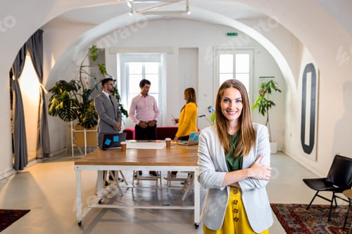 Preview: Portrait of smiling businesswoman in office with her colleagues in background.