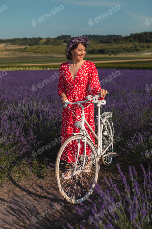 Preview: a young woman in a red dress stands with a bicycle in a lavender field