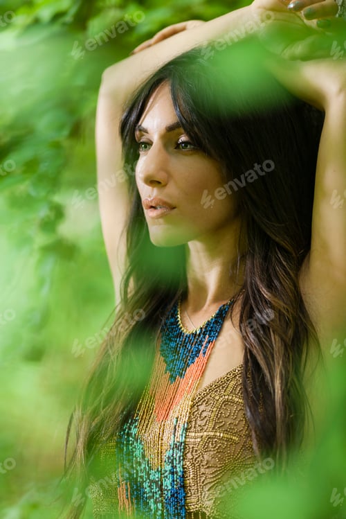 Preview: A woman with long brown hair outdoors in woodland with her arms above her head.
