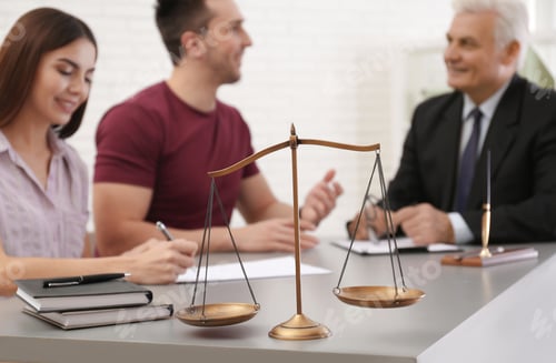 Preview: Lawyer having meeting with young couple in office, focus on scales of justice