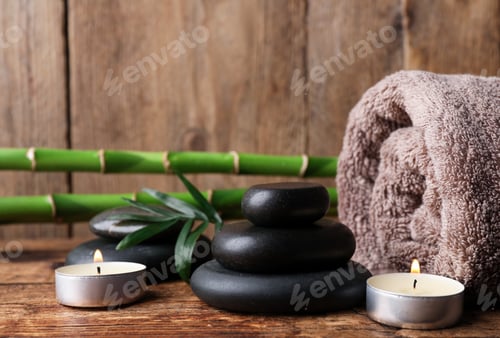 Preview: Stacked spa stones, bamboo, candles and towel on wooden table. Space for text