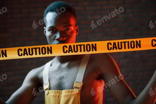 Preview: Yellow caution tape and uniform. Futuristic neon lighting. Young african american man in the studio