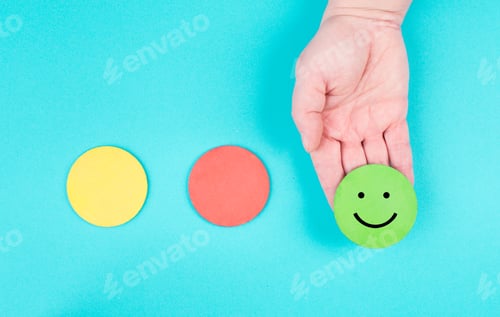 Preview: Hand holds a green smiling face, red and yellow circle empty, blue colored background, copy space