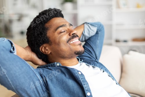 Preview: Black Man Relaxing on Couch With Hands Behind Head