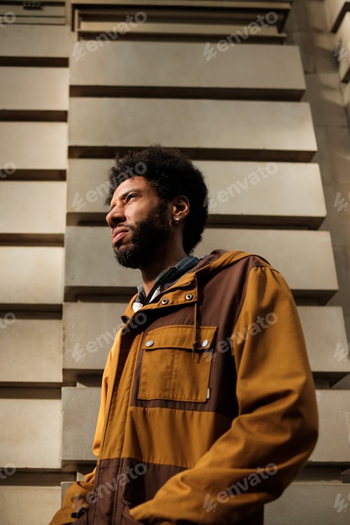 Preview: Young man wearing a brown jacket looking up in the street