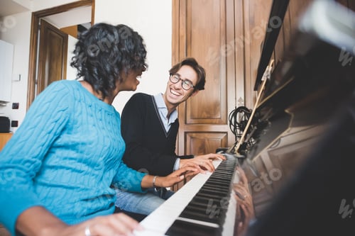 Preview: Young handsome mixed race couple in their house both playing piano