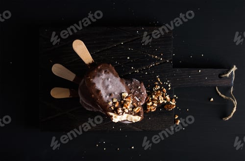Preview: Chocolate dipped popsicles with chipped nuts on dark wooden board over black background