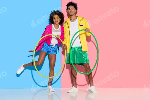 Preview: Sporty couple standing with hoops and looking to camera on pink and blue background