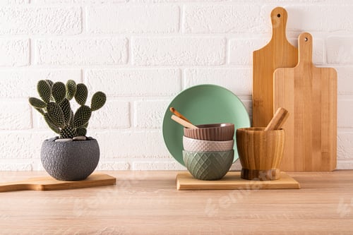 Preview: Set of ceramic bowls and cutting boards on wooden countertop in modern kitchen with potted opuntia