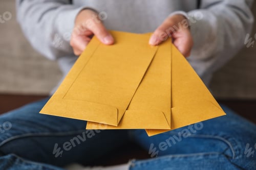 Preview: Closeup image of a woman holding and giving brown envelopes