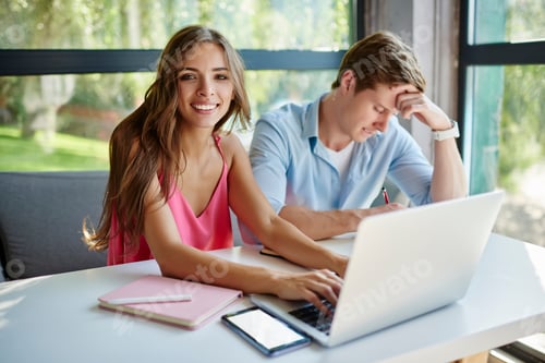 Preview: Portrait of cheerful IT professional sitting at desktop with male colleague and looking at camera