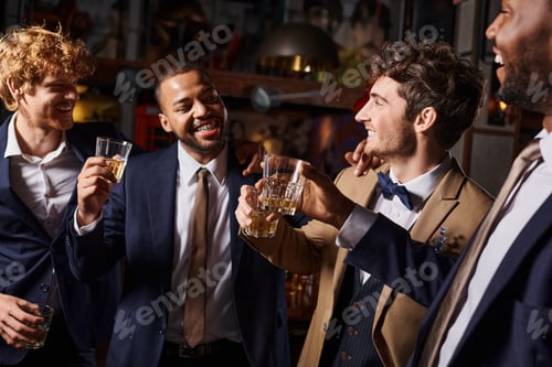 Preview: bachelor party, happy interracial men toasting with glasses of whiskey in bar, groom and best men