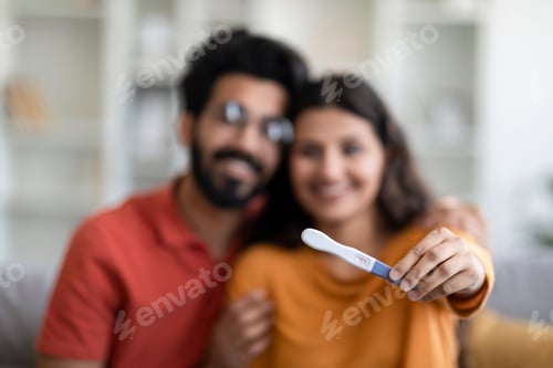 Preview: Happy indian couple showing positive pregnancy test at camera, selective focus