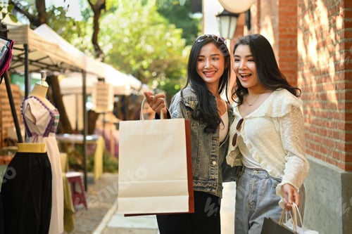 Preview: Photo of cheerful woman friends talking each other and and pointing something on the city street.