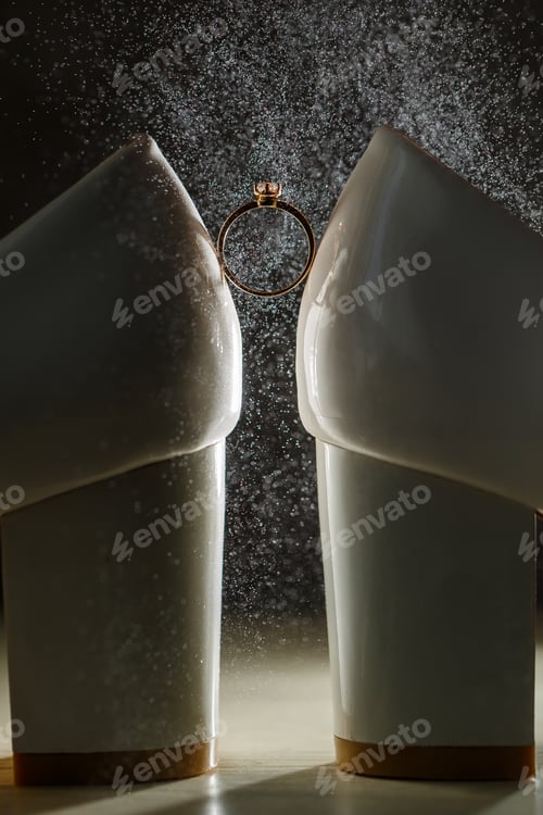Preview: Gold ring of the bride with a pebble between white shoes with heels. Bride's precious ring