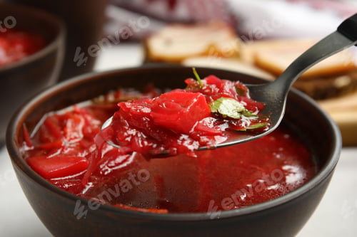 Preview: Spoon with Ukrainian borsch above stylish brown clay bowl, closeup