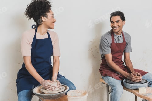 Preview: partial view of young african american couple looking at each other and modeling wet clay on wheels