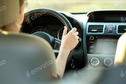 Preview: Close up view of woman holding steering wheel driving a car on city street on sunny day.