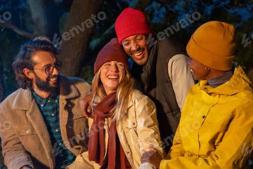 Preview: Happy diverse friends have fun laughing next to the bonfire at night caucasian and black couple.