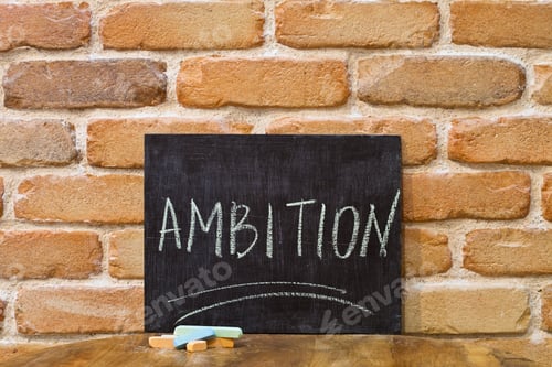 Preview: Chalk board with the word AMBITION drown by hand and chalks on wooden table on brick wall.