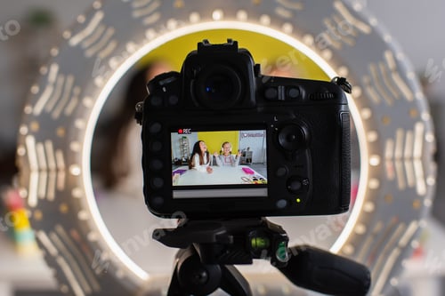 Preview: selective focus of circle lamp and digital camera with screen showing girls recording video blog