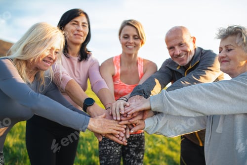 Preview: Seniors with sport instructor stacking hands after exercise outdoors in nature, active lifestyle.