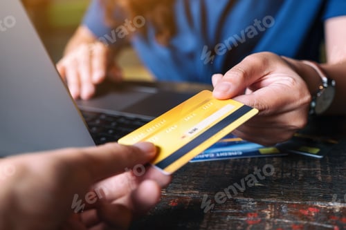 Preview: A woman holding and giving a credit card to someone while using laptop computer