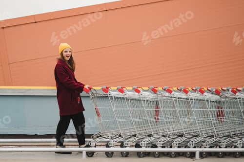 Preview: Young beautiful woman in a burgundy coat and yellow hat walks on the roof of supermarket parking lot
