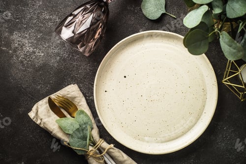 Preview: White craft plate, cutlery and green plants at black table.