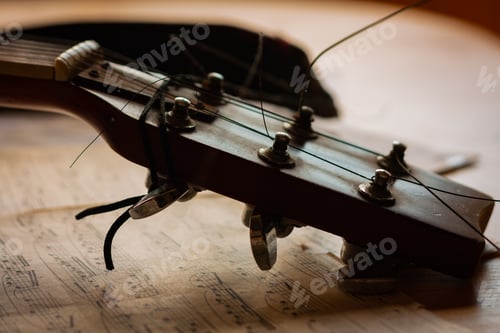 Preview: Head and tuners of acoustic guitar lying on a table on the sheets of the piece of music.