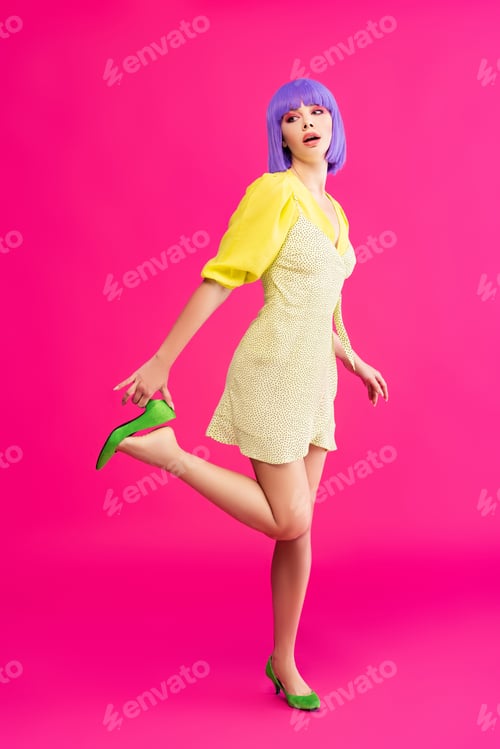 Preview: attractive pop art girl in purple wig and yellow dress posing on pink
