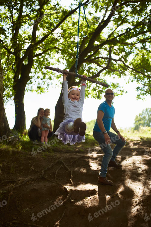 Preview: Joyful child swinging on a rope swing outdoors with family watching