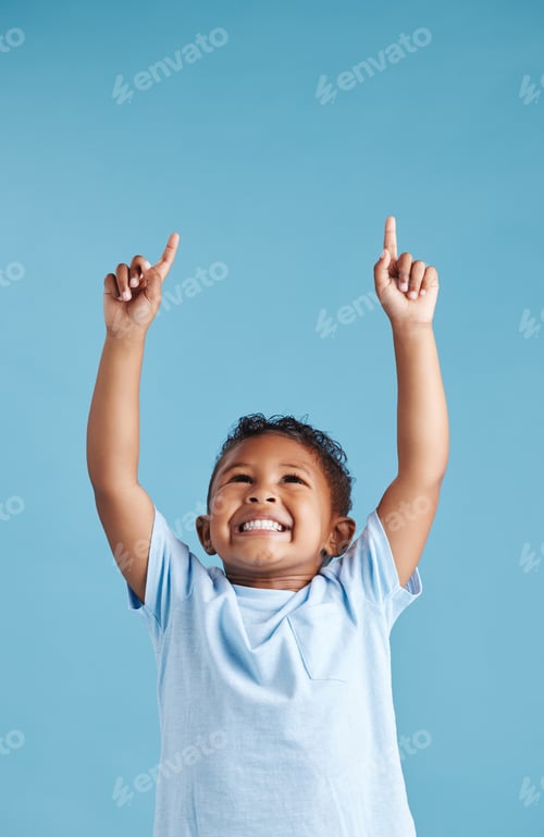 Preview: Excited little hispanic boy kid looking and pointing his fingers up at copy space against blue stud