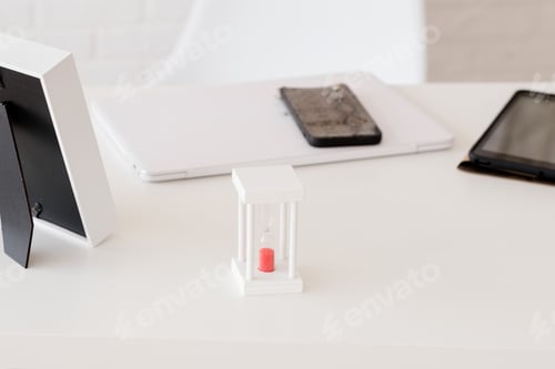 Preview: white desktop in the office, with an hourglass, against the background of a phone and a tablet