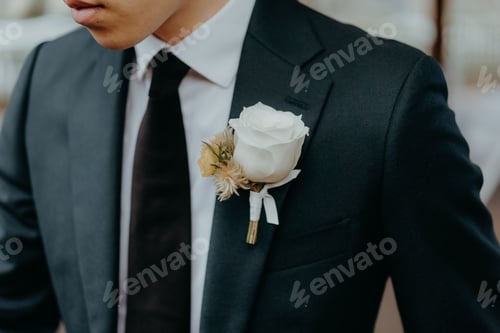 Preview: Closeup of a beautiful rose pinned to the suit of a young groom