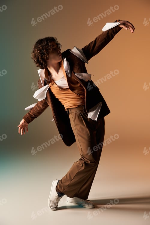 Preview: Curly-haired man in trendy outfit playfully tosses paper planes in studio